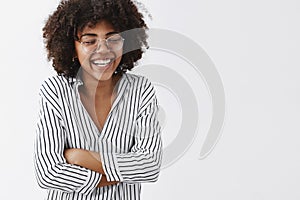 Belly aching from laughter. Amused and carefree attractive african american woman in striped blouse and glasses closing