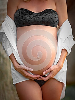 Belly of a pregnant woman. Beautiful pregnant girl. Cropped image of beautiful pregnant woman. Girl in white shirt and underwear