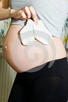 Belly of a pregnant woman holding baby socks.