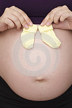 Belly of a pregnant woman, mother holding small baby socks waiting for baby