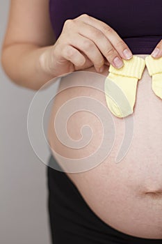 Belly of a pregnant woman, mother holding small baby socks waiting for baby