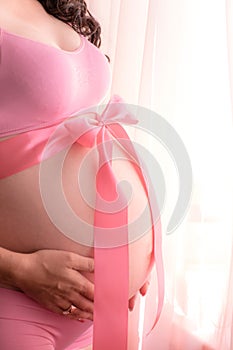 The belly of a pregnant woman. Tie with a pink ribbon with a bow