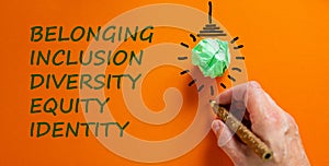 Belonging symbol. Businessman writing `identity, equity, diversity, inclusion, belonging`, orange background. Light bulb icon.