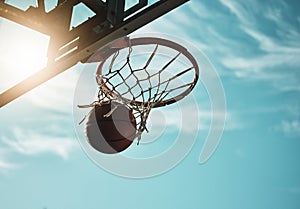 Below, basketball and net with sky in summer for shooting, scoring and points to win game. Hoop, rim and ball in closeup