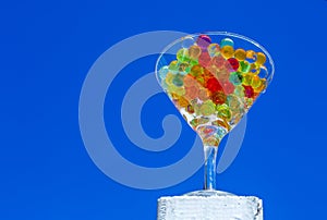 From below glass cup full of small semitransparent balls of multiple colors, with the sky as a backdrop