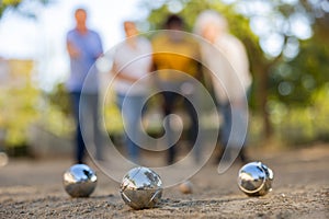 Mature casual diverse pensioners throwing petanque balls far away on a spring sunny day in the park