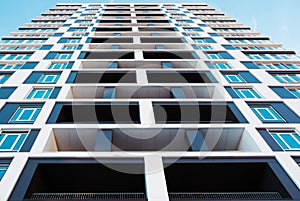 From below shot of modern and new apartment building. Photo of a tall block of flats against a blue sky.