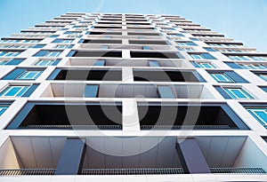 From below shot of modern and new apartment building. Photo of a tall block of flats with balconies against a blue sky.