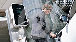 Below view closeup progressive black suit businessman recharge battery of EV car