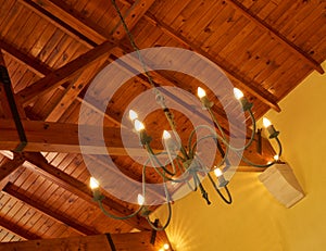 Below view of an old fashioned chandelier with candle lightbulbs hanging from sturdy wooden roof ceiling inside