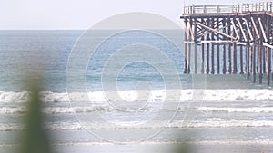 Below wooden Crystal pier on piles, ocean beach water waves, California USA.