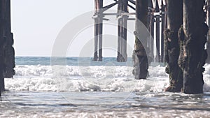 Below wooden Crystal pier on piles, ocean beach water waves, California USA.