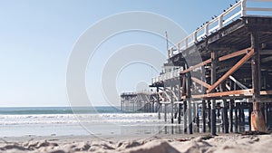 Below wooden Crystal pier on piles, ocean beach water waves, California USA.