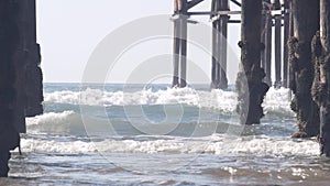 Below wooden Crystal pier on piles, ocean beach water waves, California USA.