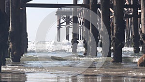 Below wooden Crystal pier on piles, ocean beach water waves, California USA.