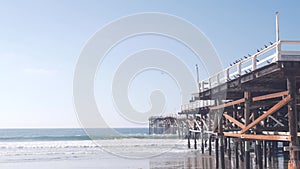 Below wooden Crystal pier on piles, ocean beach water waves, California USA.