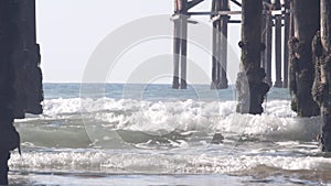 Below wooden Crystal pier on piles, ocean beach water waves, California USA.