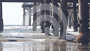 Below wooden Crystal pier on piles, ocean beach water waves, California USA.