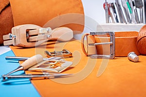 Belt buckles with leather tools on orange full grain leather background. Materials, accessories on craftman`s work desk