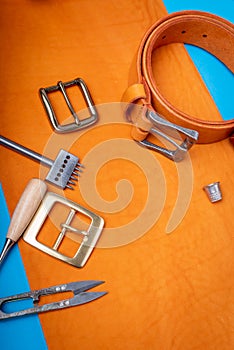 Belt buckles with leather tools on orange full grain leather background. Materials, accessories on craftman`s work desk