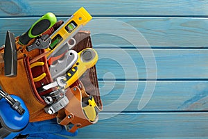 Belt with different tools on light blue wooden table, top view. Space for text