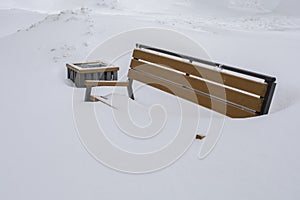 A bench in a city park completely covered with snow, winter weather, a bench hidden under a layer of snow