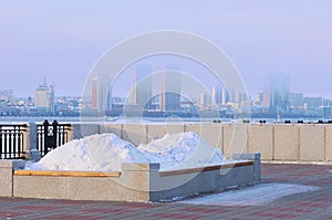 A bench with a flower bed in winter, filled with a snowdrift. Promenade of the city embankment. Blurred in the