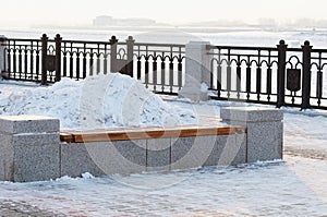 A bench with a flower bed in winter, filled with a snowdrift. Promenade of the city embankment. Blurred in the