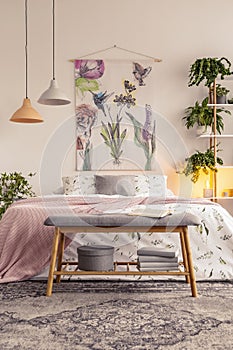 Bench with grey box and books standing by the bed with floral bedclothes and pastel pink blanket in the bright bedro photo