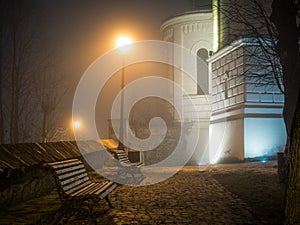 Bench illuminated by a street lamp on a foggy night, in Sighisoara Romania