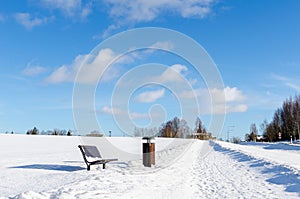 A bench and rubbish bin by a snowy road