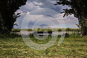 Bench by the shore of a river in the italian countryside on a cloudy day