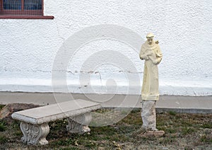 Bench and statue of a saint holding a crucifix with a dove on his left shoulder at Saint Joseph Catholic Church in Fort Davis