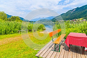 Bench with table on beach at Weissensee lake in summer landscape of Alps Mountains, Austria