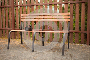 Bench, on which there is nobody. Abandoned or forgotten modern camera on the background of a wooden fence