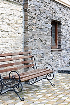 A bench with wrought-iron railings against the background of a textured stone wall of a house in the daytime