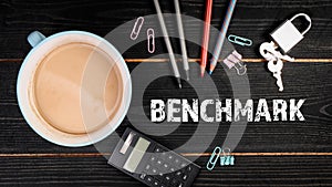 BENCHMARK. Coffee mug and office supplies on a black wood texture background