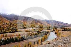 The bend of a beautiful river flowing through an autumnal valley in the mountains above which are gathering thunderclouds