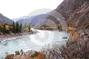 A bend of a calm mountain river flowing through an autumn valley surrounded by rocks and hills