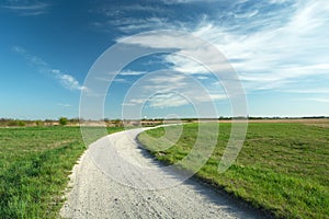 A bend on a gravel road and green meadows, white clouds on a blue sky