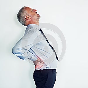 Bending over backwards to get work done. Studio shot of a mature man experiencing muscular strain.