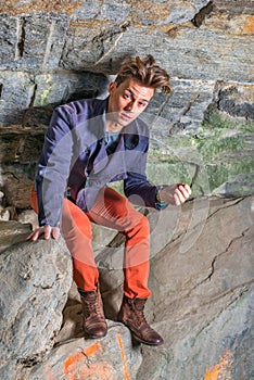 A young guy is standing in a cave of rocks, looking up, hair messed, distressful