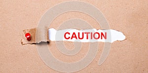 Beneath the torn strip of kraft paper attached with a red button is a white paper labeled CAUTION