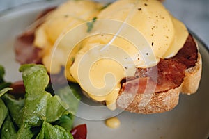 Benedict egg with bacon and salad on the white plate