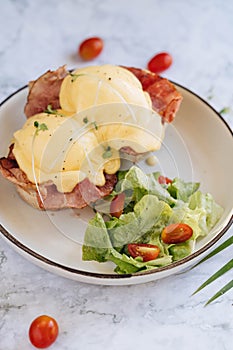 Benedict egg with bacon and salad on the white plate