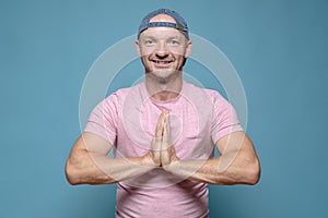 Benevolent, smiling man folded hands in a namaste gesture. Blue background.