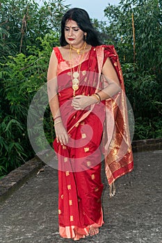 A Bengali girl wearing the red sari and golden ornaments giving poses on the roof of the forest bungalow