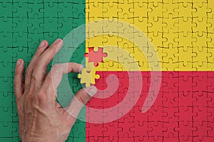 Benin flag is depicted on a puzzle, which the man`s hand completes to fold