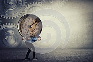 Bent down guy carrying a big heavy clock on his back. Overloaded student tired of daily tasks, and difficult burden. Time pressure photo