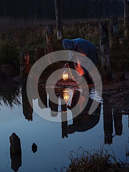 Bent man holding the old lamp outdoors near the lake. Hand holds a large lamp in the dark.  Ancient kerosene lantern illuminates